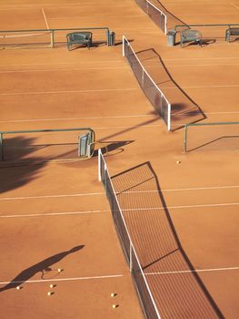 Shadow of tennis player at net with scatttered tennis balls on clay court