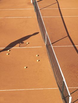 Shadow of tennis player at net with scatttered tennis balls on clay court