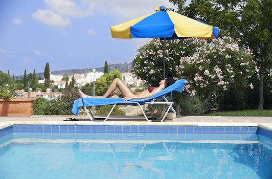 Young Woman Sunbathing In Bikini On Sunbed By Swimming Pool