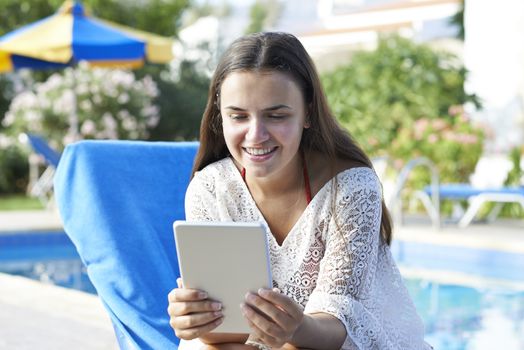 Young girl using digital tablet while relaxing by swimming pool on vacation