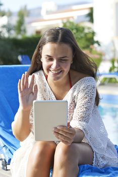 Young girl using digital tablet while relaxing by swimming pool on vacation