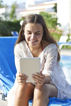 Young girl using digital tablet while relaxing by swimming pool on vacation