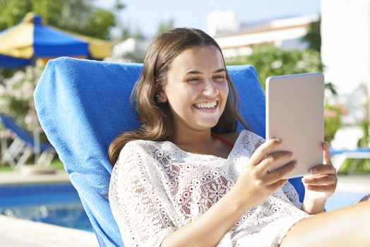 Young girl using digital tablet while relaxing by swimming pool on vacation