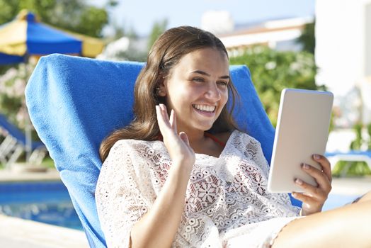 Young girl using digital tablet while relaxing by swimming pool on vacation