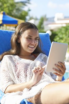 Young girl using digital tablet while relaxing by swimming pool on vacation