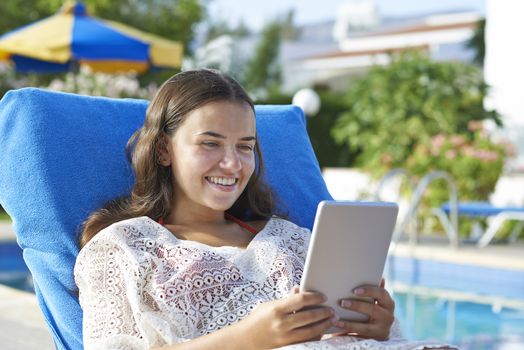 Young girl using digital tablet while relaxing by swimming pool on vacation