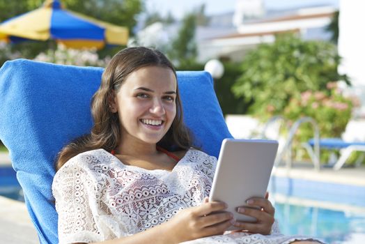 Young girl using digital tablet while relaxing by swimming pool on vacation