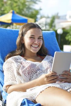 Young girl using digital tablet while relaxing by swimming pool on vacation