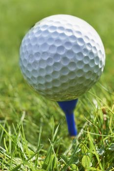 Close-up of golf ball resting on blue tee with grass and space for copy