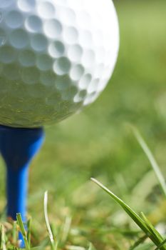 Close-up of golf ball resting on blue tee with grass and space for copy