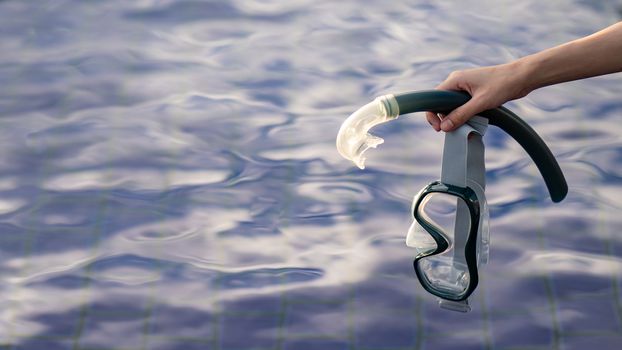 Hand with equipment for snorkeling mask at the pool.