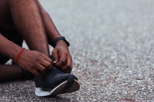 Close up Asian sport runner black man sitting shoelace trying running shoes getting ready for jogging and run at the outdoor street, health exercise workout concept