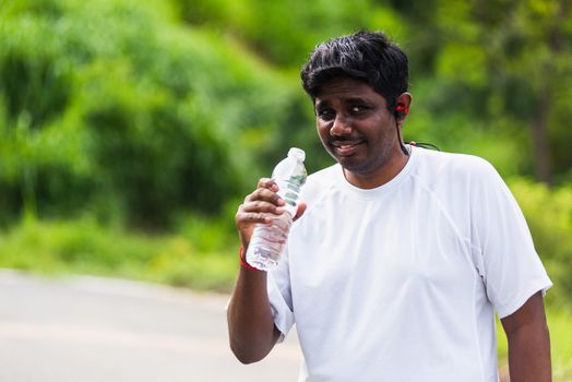 Close up Asian young sport runner black man wear athlete headphones he drinking water from a bottle after running at the outdoor street health park, healthy exercise workout concept