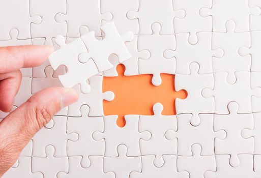 Top view flat lay of hand-holding last piece white paper jigsaw puzzle game last pieces put to place for solve problem complete mission, studio shot on an orange background, quiz calculation concept