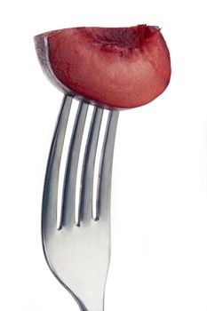 slice of plum pierced on a fork against plain background