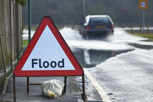 Motorist driving through flood waters with warning sign in foreground