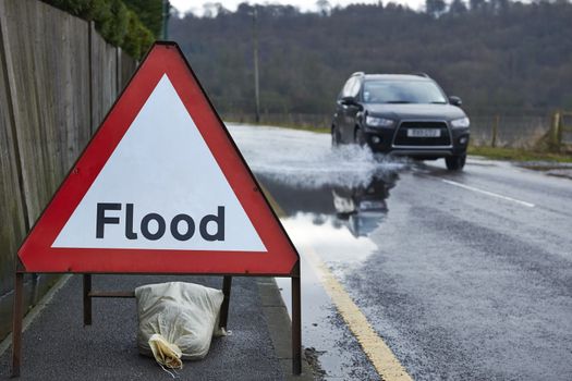 Motorist driving through flood waters with warning sign in foreground