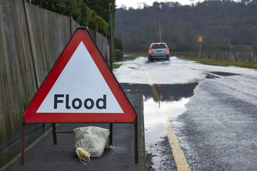Motorist driving through flood waters with warning sign in foreground