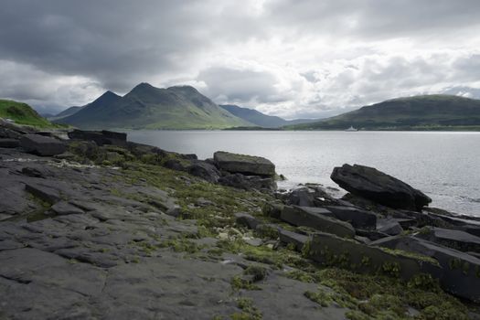 Coastal landscape from the isle of raasay looking towards the isle of skye. Ferry travels the sea under the peak of Glamaig which is cloud topped.