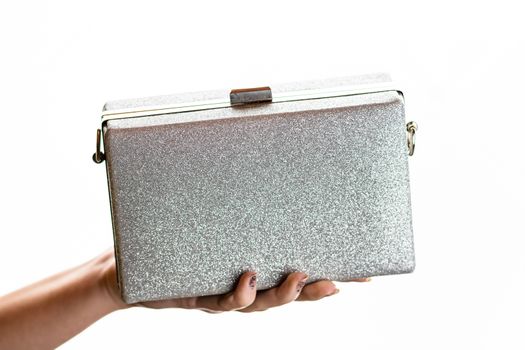 Woman hand holding glittery silver clutch bag isolated on white background with copy space.