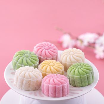 Colorful snow skin moon cake, sweet snowy mooncake, traditional savory dessert for Mid-Autumn Festival on pastel pale pink background, close up, lifestyle.