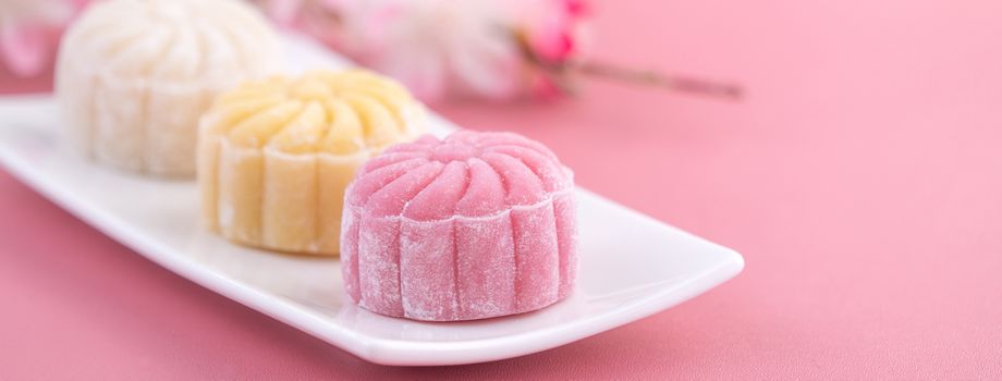 Colorful snow skin moon cake, sweet snowy mooncake, traditional savory dessert for Mid-Autumn Festival on pastel pale pink background, close up, lifestyle.