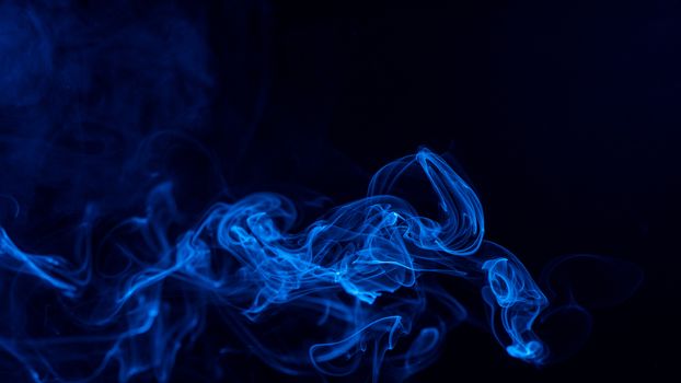 Conceptual image of blue color smoke isolated on dark black background, Halloween design element concept.