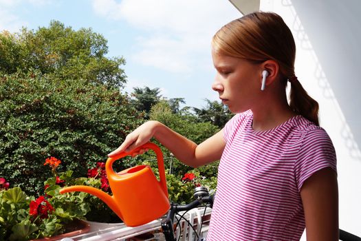 teenage girl watering flowers on the balcony from a watering can