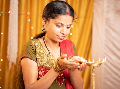 Happy smiling Indian woman lighting lantern or Diya Lamp during festival ceremony at home - concept of traditional festival and ritual celebrations.
