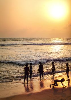 Kalutara, Sri Lanka - April 15, 2017: Silhouettes of people, mostly children playing on the beach in golden sunset evening light.
