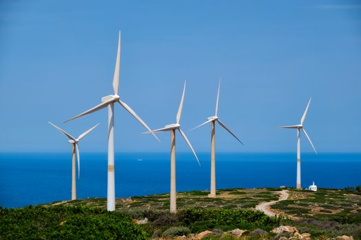 Green renewable alternative energy concept - wind generator turbines generating electricity. Wind farm on Crete island, Greece with small white church