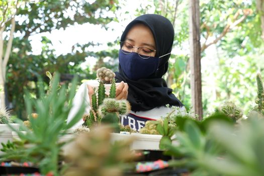 portrait of a beautiful Asian girl in a veil and wearing a mask holding a small cactus in a flower garden