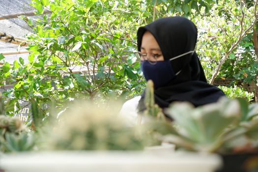 portrait of a beautiful Asian girl in a veil and wearing a mask holding a small cactus in a flower garden