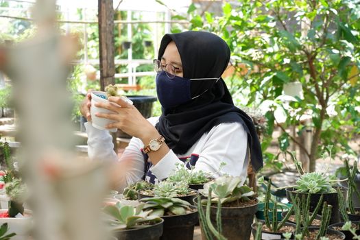 portrait of a beautiful Asian girl in a veil and wearing a mask holding a small cactus in a flower garden