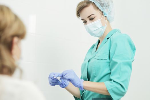 A nurse wearing a medical mask opens a disposable alcohol wipe for disinfection before taking a blood test from a patient