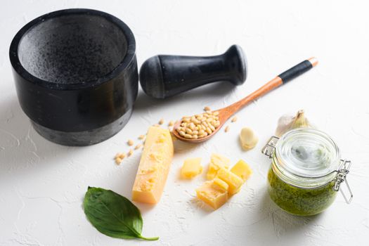 Jar of green pesto sauce on white stone table, closeup with mortar and wood spoon.