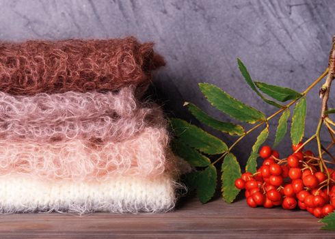 the pile of pastel wool scarves and Rowan branch on the wooden background