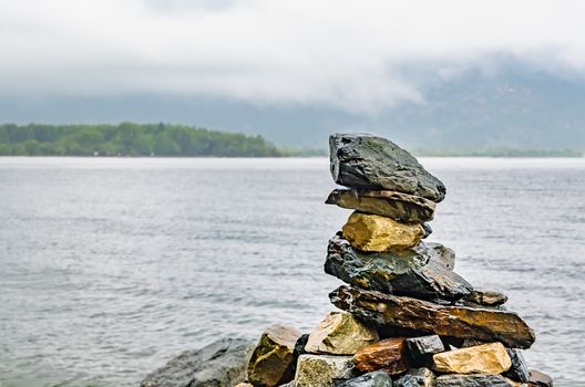 various stones stacked on top of each other in the form of a pyramid lie on the shore of the lake in foggy rainy weather