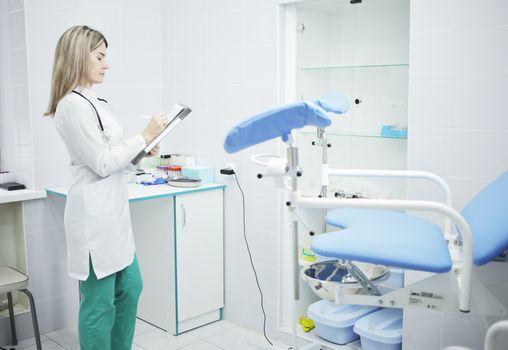 A female doctor or nurse in uniform, making notes on the medical form of the patient's medical history. Located in the gynecology office. Stethoscope phonendoscope on the neck