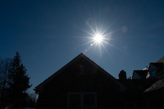 A Bright Sun Over a Silhouetted Suburban Building and Trees