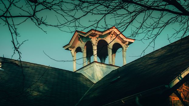 A Small White Tower With Arched Windows on a Roof With Bare Branches Surrounding the Top of the Frame