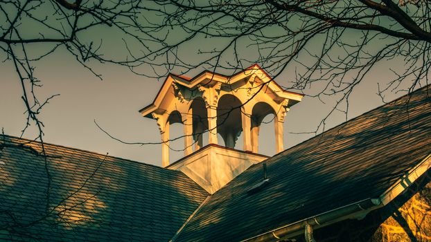 A Small White Tower With Arched Windows on a Roof With Bare Branches Surrounding the Top of the Frame