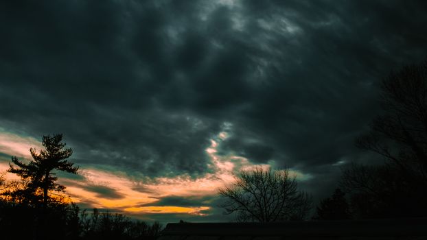 A Stormy Black and Orange Sunset With Silhouette Trees in the bottom of the frame