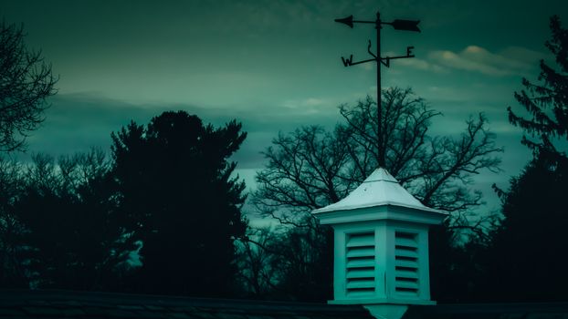 A White Wooden Tower on a Roof With a Weathervane on Top