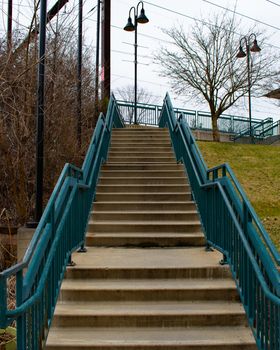 Light Concrete Steps Leading Up to a Train Station With Blue Railings on Each Side on a Cloudy Day