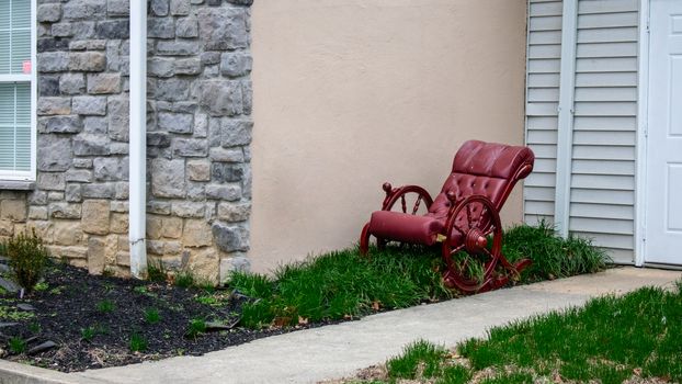 An Old-Fashioned Cushioned Red Rocking Chair Sitting in a Patch of Grass Next to a Building