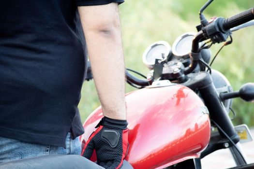 Young indian man wearing red riding gloves with protection while holding the handle bars of a motorcycle with a red tank. Shows the awareness to safety in the riding community in India