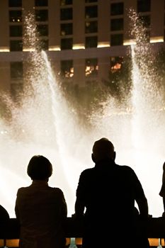 Night scene with silhouettes of people admiring the Bellagio fountains spectacle at Las Vegas