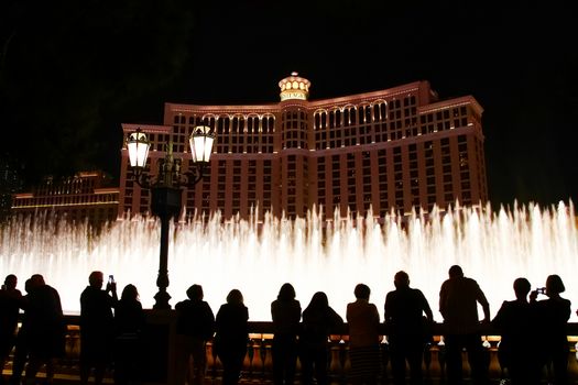 Night scene with silhouettes of people admiring the Bellagio fountains spectacle at Las Vegas