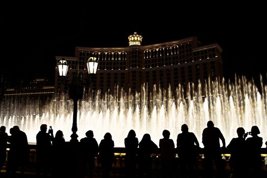 Night scene with silhouettes of people admiring the Bellagio fountains spectacle at Las Vegas